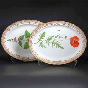 <b>Par de grandes travessas </b>ovais em porcelana dinamarquesa da importante manufatura Royal Copenhagen modelo "Flora Danica". Cada peça, inteiramente pintada à mão em belíssima policromia com suas designações botânicas e numeração no verso. Apresentam bordas em mínimos picotados cobertos a folha de ouro. Med. 45,5 x 35 cm