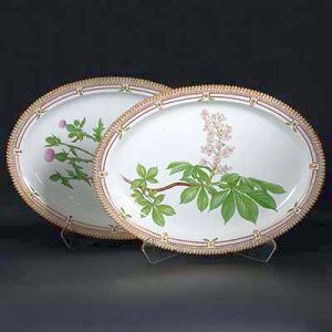 <b>Par de grandes travessas </b>ovais em porcelana dinamarquesa da importante manufatura Royal Copenhagen modelo "Flora Danica". Cada peça, inteiramente pintada à mão em belíssima policromia com suas designações botânicas e numeração no verso. Apresentam bordas em mínimos picotados cobertos a folha de ouro. Med. 53 x 39 cm
