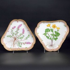 <b>Par de covilhetes </b>triangulares em porcelana dinamarquesa da importante manufatura Royal Copenhagen modelo "Flora Danica". Cada peça, inteiramente pintada à mão em belíssima policromia com suas designações botânicas e numeração no verso. Apresenta borda em mínimos picotados cobertos a folha de ouro. Compr. 21 cm