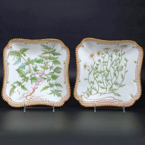 <b>Par de "bowls" </b>quadrados em porcelana dinamarquesa da importante manufatura Royal Copenhagen modelo "Flora Danica". Cada peça, inteiramente pintada à mão em belíssima policromia com suas designações botânicas e numeração no verso. Apresenta borda em mínimos picotados cobertos a folha de ouro. Med. 23 x 23 cm