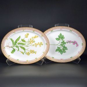 <b>Par de travessas </b>ovais em porcelana dinamarquesa da importante manufatura Royal Copenhagen modelo "Flora Danica". Cada peça, inteiramente pintada à mão em belíssima policromia com suas designações botânicas e numeração no verso. Apresenta borda em mínimos picotados cobertos a folha de ouro. Med. 40 x 31,5 cm