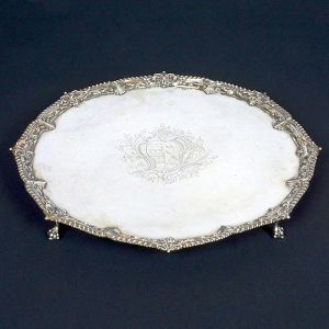 Belíssima <b>salva </b>circular em prata inglesa George III. Centro apresentando belo brasão de armas e borda levemente movimentada com gomos, "coquilles" e acantos. Pés em garras sobre bolas. Contrastes da cidade de Londres de 1782 e marca da prateira ELIZABETH JONES. Diâm. 46,5 cm. Peso 2380 gramas.