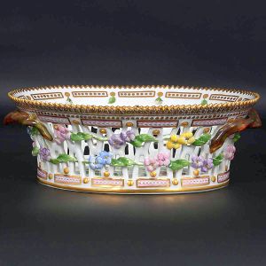 <b>Fruteira </b>oval em porcelana dinamarquesa da importante manufatura Royal Copenhagen modelo "Flora Danica". Peça inteiramente pintada à mão em belíssima policromia com suas designações botânicas e numeração no verso. Apresenta borda em mínimos picotados cobertos a folha de ouro. Med. 23 x 18,5 cm