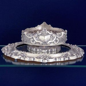 <b>Centro de mesa </b>em prata portuguesa profusamente decorada com composições de flores, volutas, acantos e "coquilles" no estilo D. João V. Base espelhada ao centro. Contrastes da cidade do Porto, 833 ml, usado a partir de 1938. Compr. da floreira 28 cm; Compr. da base 51 cm. Peso 2335 gramas.