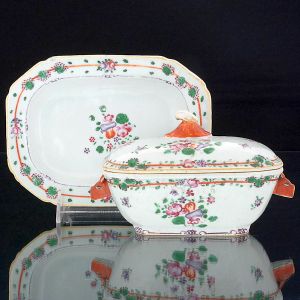 <b>Terrina para molho e seu "presentoir" </b>em porcelana Companhia das Índias decorada com flores e frutos nos esmaltes da Família Rosa. Pegas do bojo modelada em cabeças de lebre em "rouge de fer" e da tampa em folhagens. Séc. XVIII. Compr. da terrina 18 cm; Compr. do "presentoir" 19,5 cm