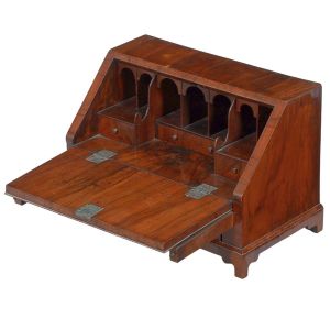 <b>Papeleira miniatura</b>  inglesa George III em raiz de nogueira. Tampo reclinável com apoio sobre duas traves laterais. Interior dividido em escaninhos em forma de arcada e três gavetinhas. Parte inferior com gaveta de maior tamanho. Acompanha chave original. Med. fechada 31 x 48 x 27 cm