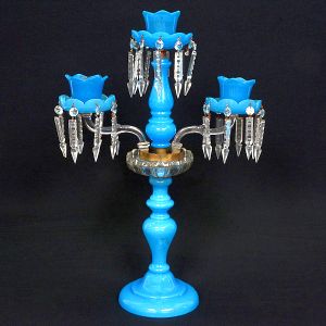 <b>Candelabro para três luzes </b>em opalina francesa. Apresenta base circular, haste em segmentos de balaústre, com aparato ao centro, onde assentam-se par de braços ondulados com receptáculos em forma de tulipa. Pingentes em cristal Baccarat lapidado em ponteiras. Séc. XIX. Alt. 57 cm