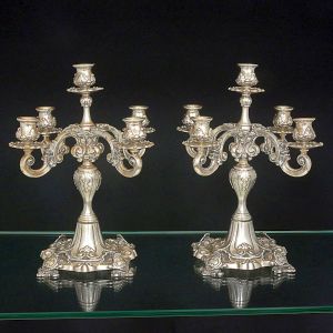 <b>Par de candelabros </b>em prata 833 ml, para cinco velas, e profusa decoração com elementos característicos do estilo D. João V com braços em curva e contracurva sustentando os receptáculos recamados por folhas. Bases quadradas. Marca do prateiro CORREA. Alt. 35 cm. Peso 4125 gramas.