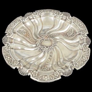 <b>Medalhão </b>em prata portuguesa de forma circular. Aba em recortados com segmentos floridos intercalados por concheados. Centro retorcido decorado com os mesmos motivos e reserva ao centro. Contraste "Javali" usado de 1886 a 1938 e marca de prateiro. Diâm. 44,5 cm. Peso 820 gramas.