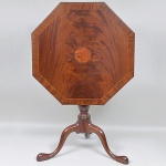 Antiga <b>mesa de apoio </b>inglesa construída em madeiras nobres no sistema dito "tilt top". Tampo de forma octogonal circundado por frisos e ao centro reserva em raiz de nogueira. Coluna central torneada e triplos pés recurvados terminados em pés de sapatas. Med. 67 x 66,5 x 66,5 cm
