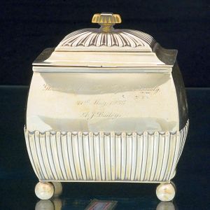 <b>Caixa de chá </b>em prata inglesa vitoriana decorada com gomos a meia altura e tampa com pega em marfim e pés de bola. Inscrições na face anterior. Contraste da cidade de Londres 1895 e marca do prateiro HENRY WILLIAN Son & Cº. Med. 13,5 x 11 x 8,5 cm. Peso 265 gramas.