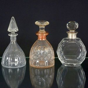 <b>Conjunto de três garrafas </b>em cristal com lapidações diversas. Composto por garrafa de corpo facetado com tampa piramidal, outra com detalhes lapidados e friso superior em metal dourado e a terceira com lapidação geométrica em corpo octogonal com tampa facetada.