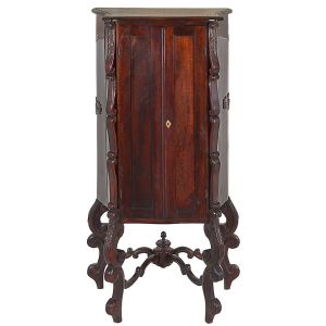 <b>Armário </b>luso brasileiro em Jacarandá apresentando duas portas rebatíveis e ilhargas e pés movimentados com entalhes em discretas volutas. Amarração inferior em traves unidas por carrapetas na parte posterior. Interior com três prateleiras. Med. 150 x 78 x 51 cm