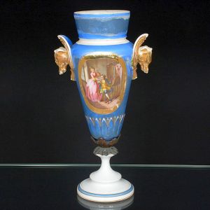 Antiga <b>ânfora </b>ornamental em porcelana francesa ao gosto de Sèvres com base em pedestal branco unida ao bojo por elemento em bronze, provavelmente com restauro. Reserva com cena galante e alças em cabeça de cachorros. Realces a ouro. Alt. 38,5 cm