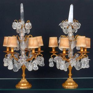 <b>Par de girandoles</b>, com bases em bronze dourado finamente moldado e estrutura superior ricamente ornamentada com pingentes, gotas e elementos lapidados em cristal. Braços com "bobèches" metálicas, decoradas com pequenas cúpulas em tecido. Alt. 71 cm