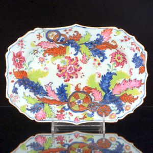 <b>Travessa </b>de forma retangular e cantos chanfrados em porcelana Companhia das Índias decorada em rica policromia florida no padrão "Folha de Chá". Predominância das tonalidades de rosa, azul, verde e "rouge de fer". Séc. XVIII. Med. 26,5 x 18,5 cm