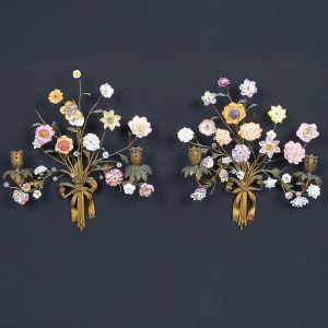 <b>Par de apliques</b>, com estrutura em metal dourado trabalhado em forma de ramos entrelaçados, finalizados por laços na base. Decorados com flores modeladas em porcelana policromada, em tons suaves e variados, compondo arranjo. Alt. 39 cm