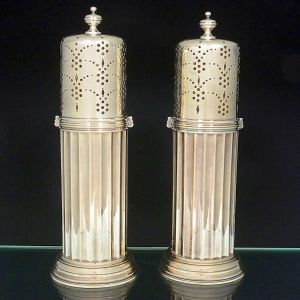 <b>Par de grandes polvilhadores </b>em prata inglesa decorada em gomos escavados e base circular frisada. Pega da tampa em forma de pinha. Contraste da cidade de Londres de 1978 e marca do prateiro CGV Ltda. Alt. 37,5 cm. Peso 2590 gramas.