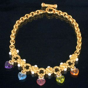 <b>Colar </b>em ouro 18k com pérolas de 6 mm e cinco corações em formato de "cabochons" de ametista lilás, topázio azul, turmalina rosa, "peridot" verde e citrino amarelo com o peso aproximado de 30,00 ct. Peso total da peça 96,57 gramas.