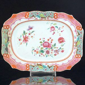 <B>Travessa </B>de formato retangular com cantos chanfrados, em porcelana Companhia das Índias decorada em esmaltes policromados da Família Rosa com composições florais e frisos geometrizados. Reinado Qianlong (1736-1795). Compr. 30,5 cm