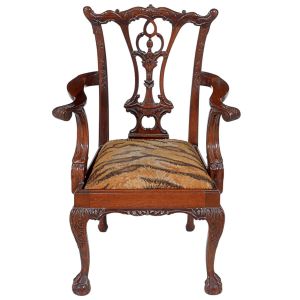 Antiga e <b>pequena cadeira baixa </b>inglesa do estilo "Chippendale". Apresenta espaldar vazado com entalhes vegetais, braços sinuosos e pernas em "en cabriolet" terminadas em garras sobre esferas. Assento em "animal print". Alt. 65 cm