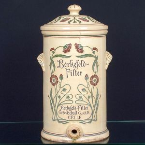 Antigo <b>filtro </b>em cerâmica alemã esmaltada, decorada na parte frontal com motivos florais estilizados em relevo e inscrições. Marca Berkefeld-Filter Gesellschaft GmbH, Celle. Possui tampa e saída inferior para torneira (ausente).