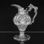 Grande <b>jarra </b>em prata portuguesa apresentando corpo bojudo implantado em elementos fitomórficos e alça recurvada. Decoração no estilo D. João V. Monograma à frente. Aparentemente sem marcas. Alt. 30 cm. Peso 1305 gramas.