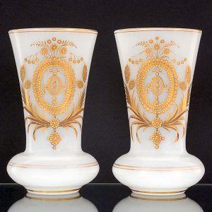 <b>Par de vasos </b>em opalina francesa Baccarat na cor branco leitoso, apresentando parte inferior bojuda e haste na forma de tulipa. Bela decoração com medalhões, motivos neoclássicos e frisos a ouro. Séc. XIX. Alt. 30 cm