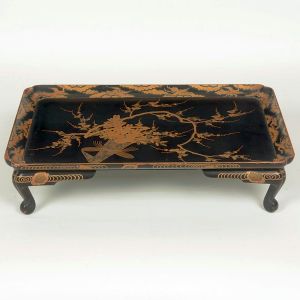 <B>Mesa-bandeja </B>retangular, em laca preta com decoração oriental em dourado, representando ramos floridos, aves e elementos paisagísticos finamente detalhados, apoiada sobre quatro pés recurvados. Med. 48,5 x 33,5 cm