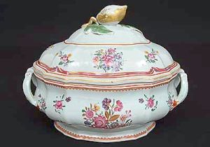 <B>Sopeira </B>de forma oblonga, ao gosto das peças de Meissen, decorada em rica policromia florida predominando tonalidade de rosa e violeta. Pega da tampa modelada em fruto e realces a ouro. Séc. XVIII. Compr. 33 cm