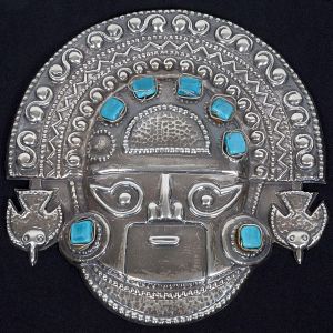 <b>Máscara decorativa </b>em prata teor 925 ml, com rica gravação geométrica, motivos de aves estilizadas nas laterais e elementos simbólicos em relevo. Apresenta aplicações de pedra em tom turquesa. Med. 18 x 18 cm