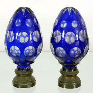 Antigo <b>par de pinhas </b>francesas em cristal, ornamentadas em "overlay" azul cobalto, com elementos circulares e estrelado ao topo. Base em bronze de época. Uma delas com trincado na base. Séc. XIX. Alt. 20 cm