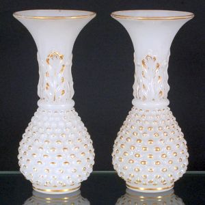 <b>Par de vasos </b>franceses em opalina branco leitoso. Apresentam parte inferior bojuda decorada a ouro com elementos ovais em relevo. Haste com folha de palma e bocal de corneta filetado. Séc. XIX. Alt. 25 cm