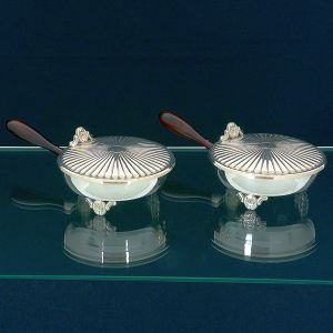 <b>Par de pega migalhas / cinzas </b>em metal espessurado a prata italiana. Decoração em gomos, pés e pega da tampa em "coquilles" e alças em madeira torneada. Marca do fabricante no verso. Compr. 27,5 cm