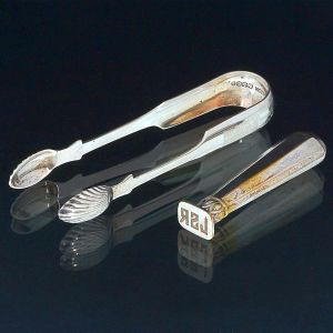 <b>Conjunto </b>de: a) Pegador de gelo em prata escocesa (Edimburgo, 1935) com marca do prateiro M & C. Compr. 14 cm; b) Sinete com iniciais JSR aparentemente sem marcas. Alt. 9,5 cm. Peso 95 gramas.