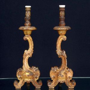 <b>Par de "abatjours" </b>esculpidos em madeira, apresentando volutas, concheados e base tripartida em movimentos sinuosos. Fuste torneado na parte superior, onde se encontra o bocal. Alt. 57 cm