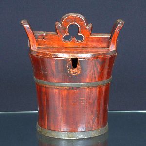 <B>Balde </B>oriental em madeira com bela pátina avermelhada e aros metálicos de reforço. Corpo cilíndrico levemente abaulado, com tampa articulada e dobradiça dianteira em ressalto. Alt. 32 cm