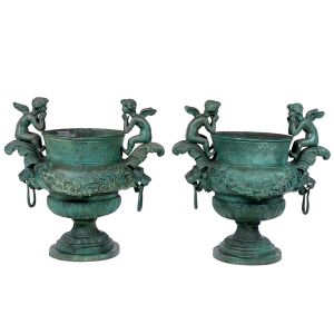 <b>Par de "cachepots" </b>bojudos, em bronze, decorados com guirlandas florais, folhagens e figuras de "puttis" alados. Base torneada, em formato de campânula, com friso decorativo.