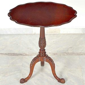 Pequena <b>mesa auxiliar </b>em mogno apresentando tampo de aba ondulatória apoiado em coluna central e triplos pés entalhados com folhas. Pés em garras. Med. 61 x 56,5 cm