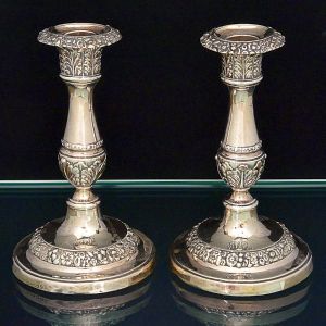 <b>Par de castiçais </b>em prata inglesa, do período George IV. Haste em segmentos de balaústre circular e decoração com flores e folhas. Contraste da cidade de Sheffield de 1823 e marca do prateiro John & Thomas Settle. Alt. 18,5 cm