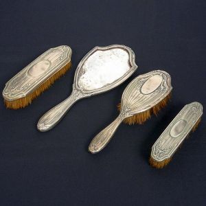 <b>Conjunto de 3 escovas e 1 espelho </b>de "toilette" em alpaca com decoração de frisos e guilhochadas. Apresenta mossas. Compr. do espelho 29 cm