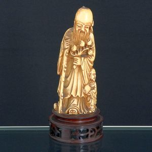 <b>Estatueta </b>chinesa em marfim esculpido representando figura de ancião com criança. Ponta do cajado quebrada. Base em madeira. Alt. 19,5 cm