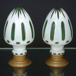 <B>Par de pinhas </B>ornamentadas em cristal "overlay" verde, com cortes verticais. Pedestal circular em metal dourado. Alt. 21 cm