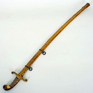 <b>Espada </b>com bainha, ricamente trabalhada em metal dourado, com cabo, guarda e bainha ornamentados por motivos florais em relevo. Lâmina curva com damasquinagem em ouro, apresentando figuras e arabescos ao longo de toda a extensão. Desgastes naturais do tempo.