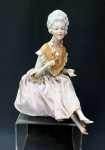 Antiga e delicada boneca sentada c/ vestes originais em porcelana alemã dita "Half Doll" década de 20/30 em base forrada. Pernas cruzadas em delicado movimento sapatos de salto com vestígios de dourado, Corpo com decote em babados tendo flores nas mãos. Obs: falta dedinho polegar. Altura de 19 cm e base de 11 cm de diâmetro.