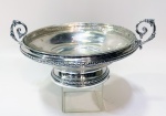Delicada cesta em prata teor 800 contrastada, estilo fruteira para confeitos peso de 222 g, tendo nas laterais alças ricamente trabalhadas em volutas e folhas. Frisos cinzelados e parte superior com recipiente em cristal c/ 2 mínimos bicados na borda. Altura de 9 cm.