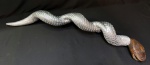 Escultura de cobra em madeira de raiz pintura em prata realçando as escamas da pele da cobra. Tem 2ª cabeça em madeira natural representando "cobra engolindo cobra". Mede 88 cm.