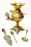 Samovar em metal dourado com base de 4 apoios curvos, detalhes em frutas e torneira feitio de cabeça de pássaro, falta a tampa e mede 21 cm de altura. Acompanham 3 peças em metal cinzelado sendo 1 espátula de alça curva com vazados de 16 cm, 1 concha de cabo em flor medindo 15 cm e 1 colher para açucar com 12 cm.