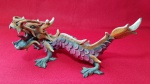 Dragão feito em resina sintética, com bonita policromia, apresenta perda de um chifre e um dedo, conforme fotos - Dimensão: 26 X 12 cm