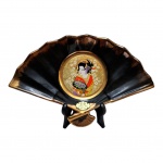 COLECIONISMO - The Art of Chokin, peça em porcelana representando leque com medalhão central representando figura feminina, bordas negras em `ouro` 24, na parte posterior elucidação sobre a arte, 25 x 16 cm.